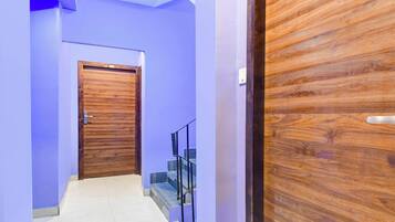 Un pasillo con una puerta de madera, una escalera con barandilla de metal y un interruptor de luz en la pared.