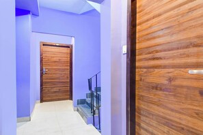 Un pasillo con una puerta de madera, una escalera con barandilla de metal y un interruptor de luz en la pared.
