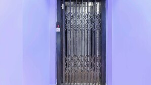 Una puerta con una reja metálica y un panel de control con una luz roja.