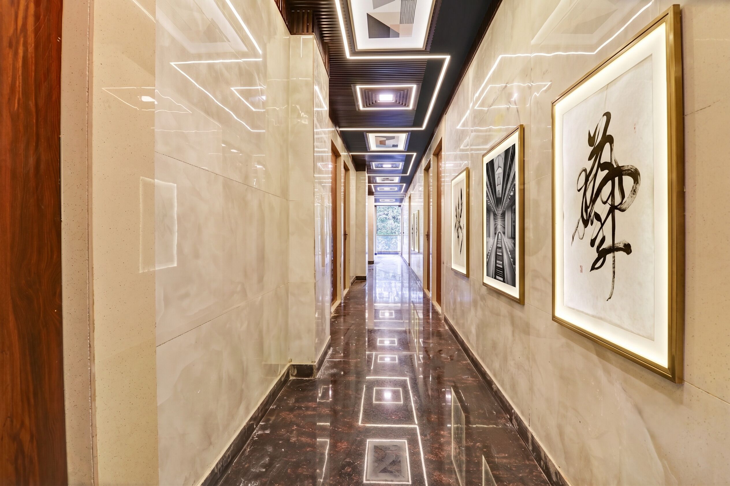 A hallway with a polished marble floor, framed artwork on the walls, and a modern ceiling design with recessed lighting.