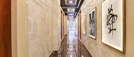A hallway with a polished marble floor, framed artwork on the walls, and a modern ceiling design with recessed lighting.