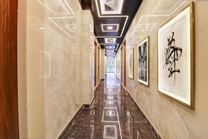 A hallway with a polished marble floor, framed artwork on the walls, and a modern ceiling design with recessed lighting.