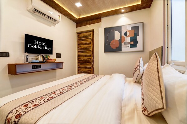 A hotel room with a bed, a flat-screen TV displaying 'Hotel Golden Key', a wall-mounted shelf with amenities, and a modern abstract painting.