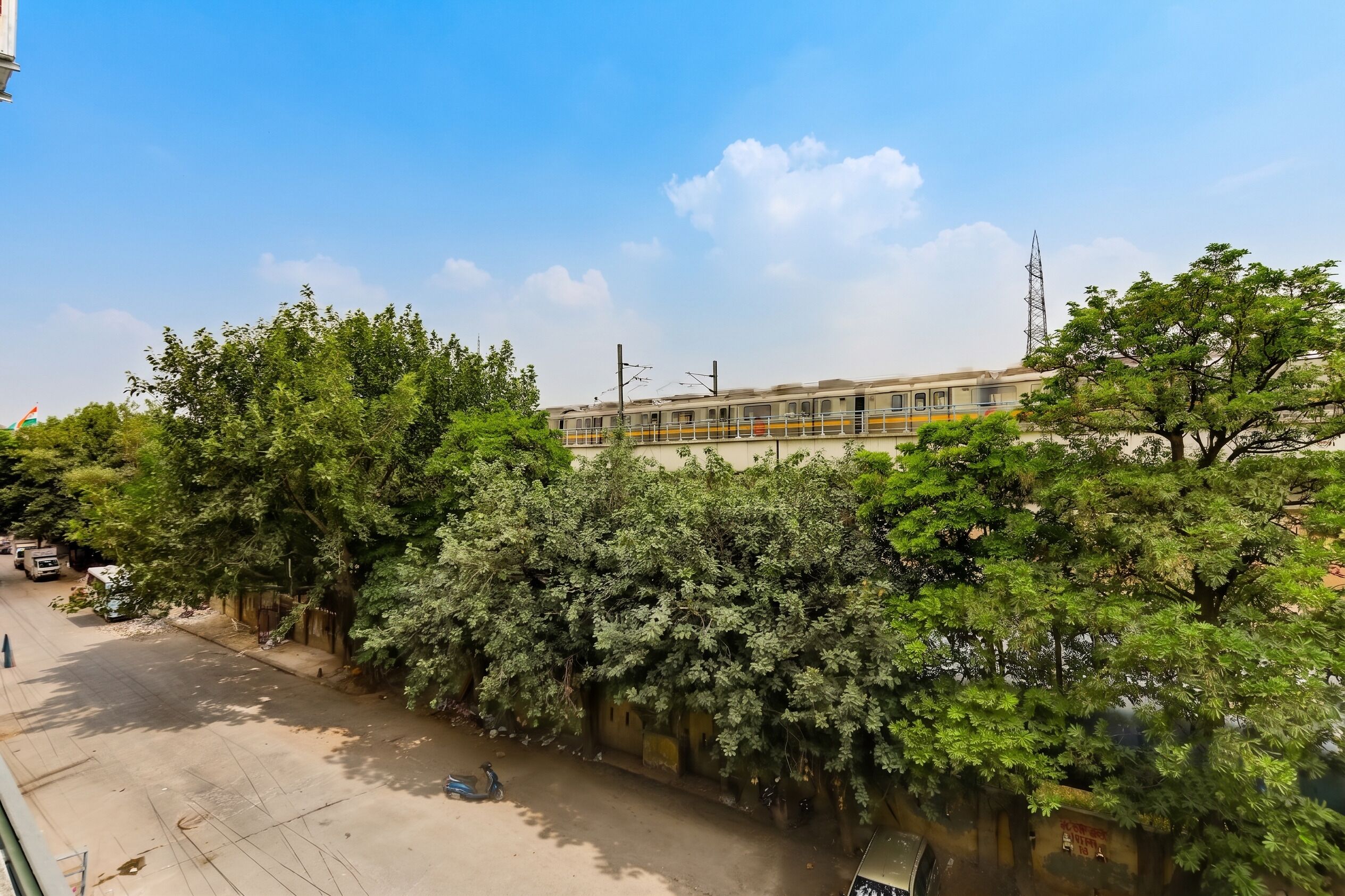 A street with a train passing by, trees lining the road, and a clear sky.