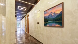 A hallway with a marble floor, a painting of a mountain landscape, and a ceiling with recessed lighting.