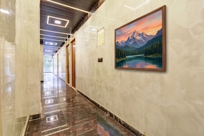 A hallway with a marble floor, a painting of a mountain landscape, and a ceiling with recessed lighting.
