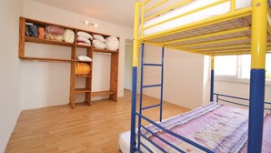 A bunk bed with a wooden ladder and a shelf unit with pillows and folded blankets.