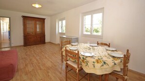 A dining area with a round table set for four, wooden chairs, a floral tablecloth, and a large wooden cabinet in the background.
