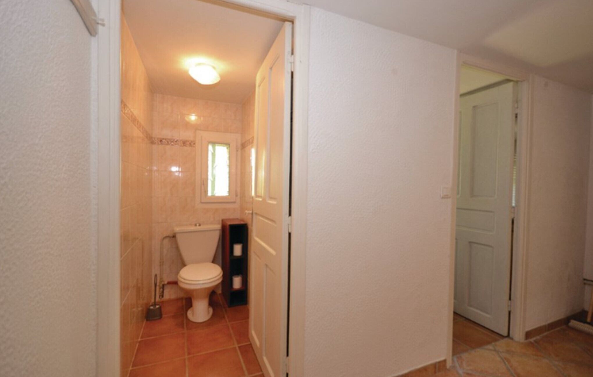 A bathroom with a toilet, a small window, and a door leading to another room.