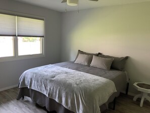A bedroom with a bed, a nightstand, a window with blinds, and a ceiling fan.