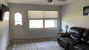 A living room with a black leather sofa, a ceiling fan, a window with blinds, and a door. - Newly remodeled. Quiet neighborhood 4 blocks from iconic Sturgis mainstreet (Sturgis)
