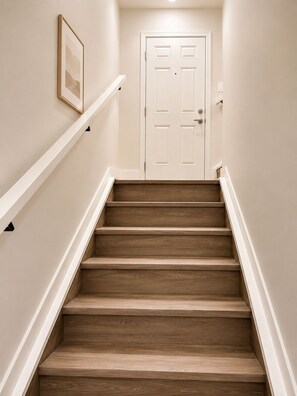 A staircase with wooden steps and white handrails, leading to a white door with a handle. - Cozy & Fully Furnished 2-bedroom Basement Suite (Edmonton)