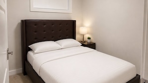 Uma cama bem arrumada com cabeceira, uma luminária de cabeceira e um quadro na parede.