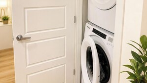 Uma lavanderia com duas máquinas de lavar empilhadas e uma porta branca.