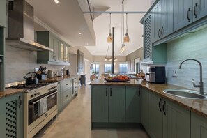 A modern kitchen with a central island, stainless steel appliances, and a view to the outdoors. - Sunhaven at Pezula (Knysna)