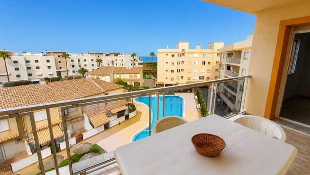 Ein Balkon mit Tisch und Stühlen, der einen Blick auf ein Schwimmbad und Wohnhäuser bietet.