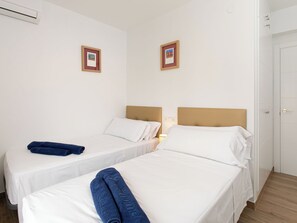 Een hotelkamer met twee éénpersoonsbedden, een witte muur, een deur en een klein, lijstwerk afgewerkt foto aan de muur.