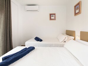 A hotel room with two beds, a window with curtains, an air conditioning unit, and a framed picture on the wall. - Elvix Nerja Centre B by Interhome (Nerja)