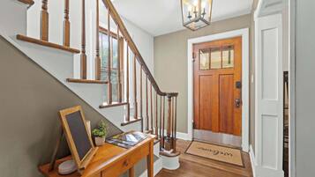 A wooden staircase with a handrail, a desk with a chalkboard, a potted plant, and a welcome mat.