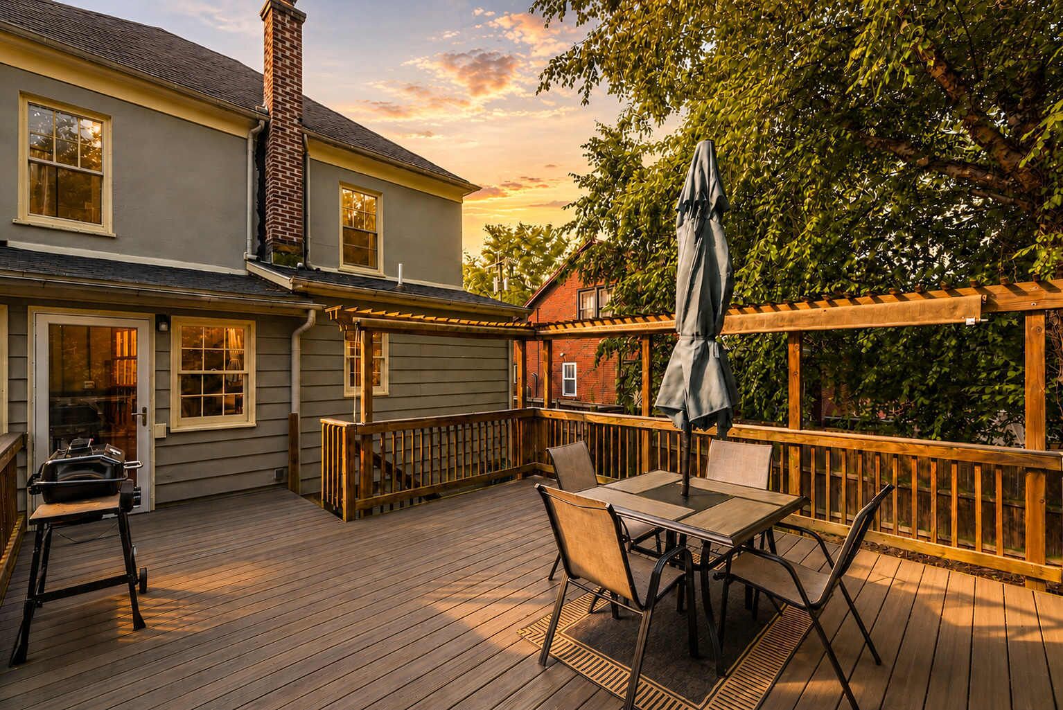 A wooden deck with a table and chairs, a grill, and a pergola with an umbrella.