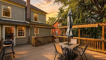 A wooden deck with a table and chairs, a grill, and a pergola with an umbrella.