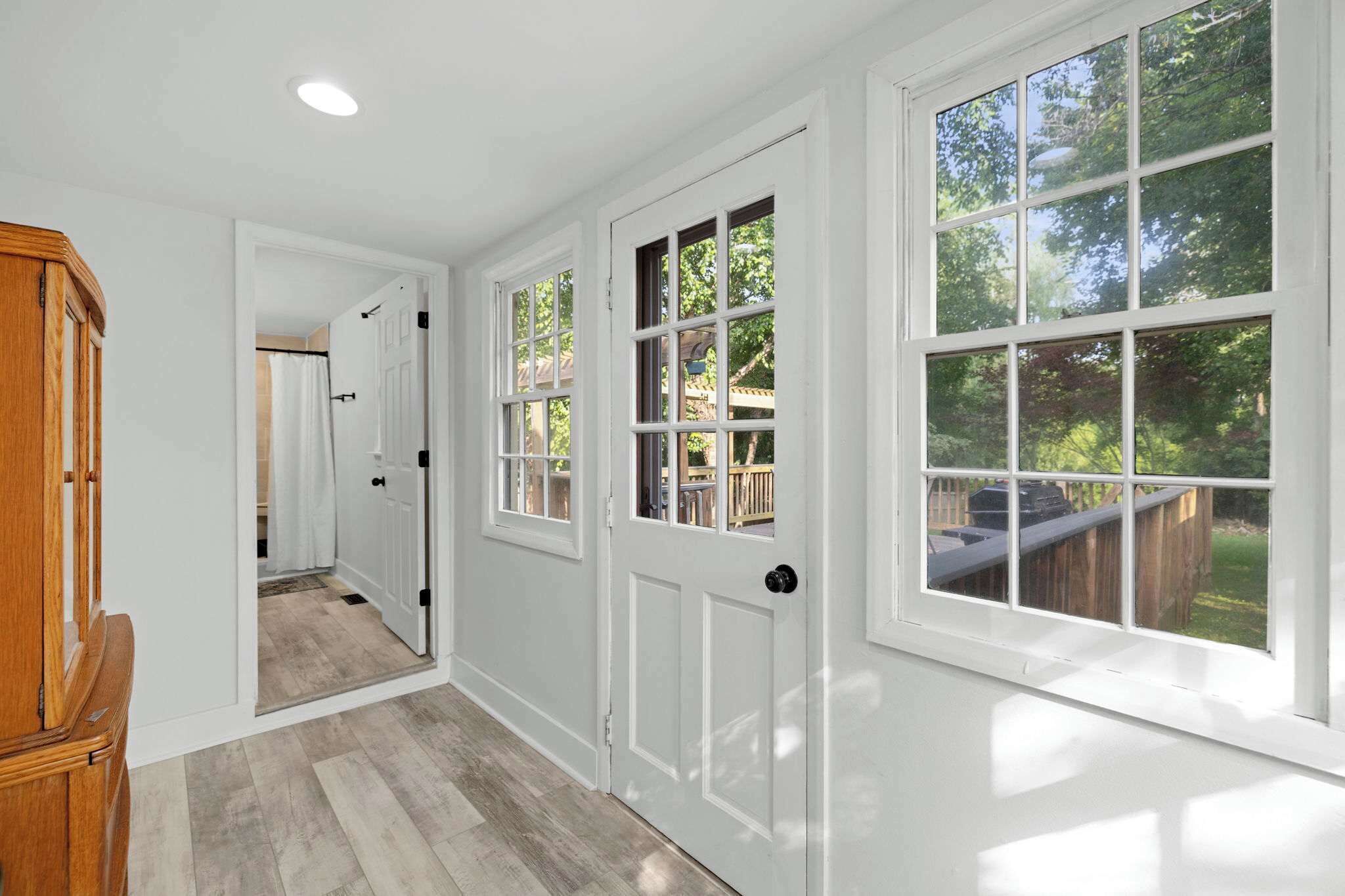 A hallway with white walls, wooden doors, and large windows with a view of the outdoors.