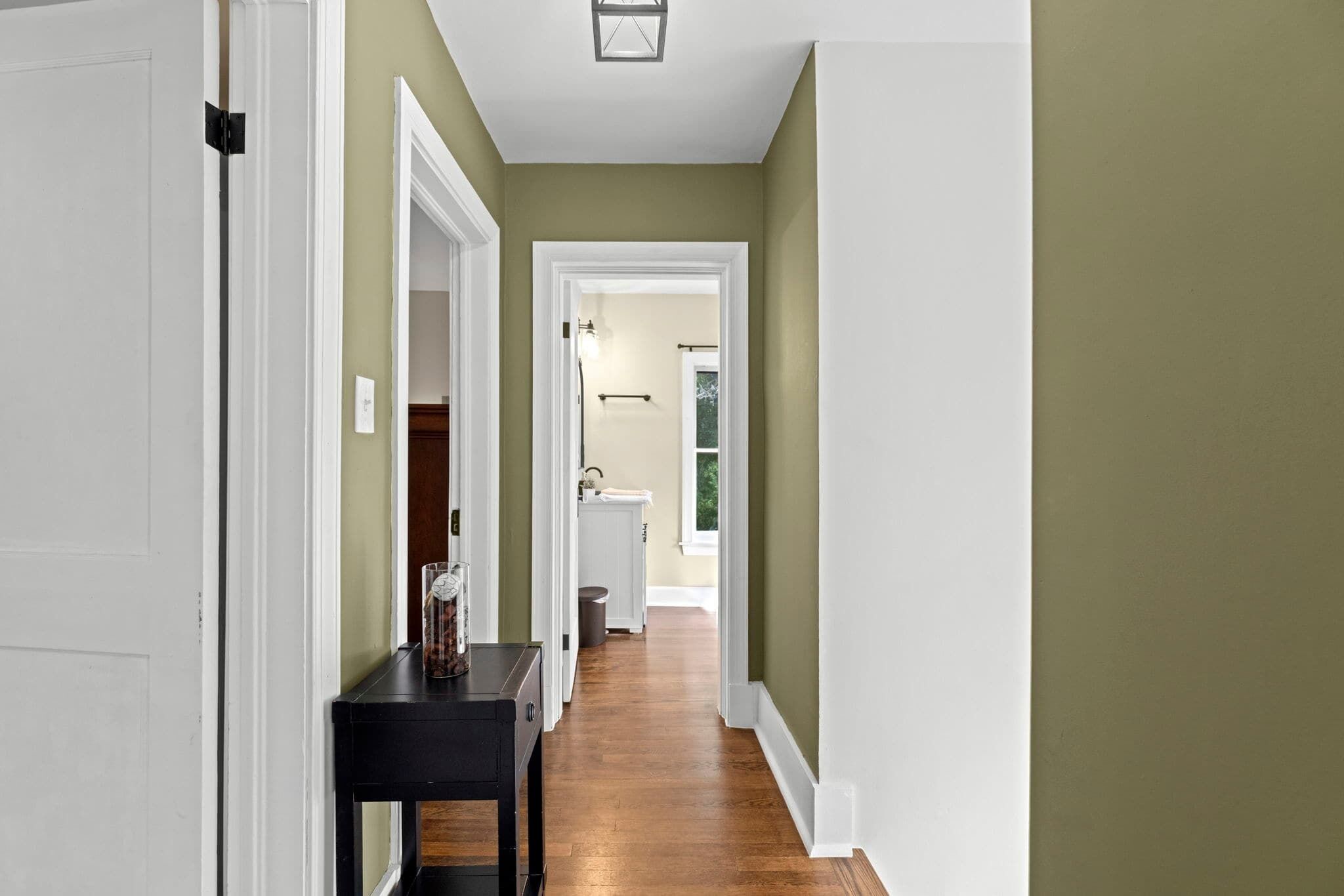 A hallway with a wooden floor, white trim, and a door on the left.