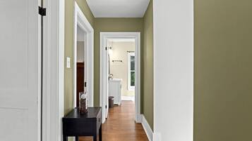 A hallway with a wooden floor, white trim, and a door on the left.