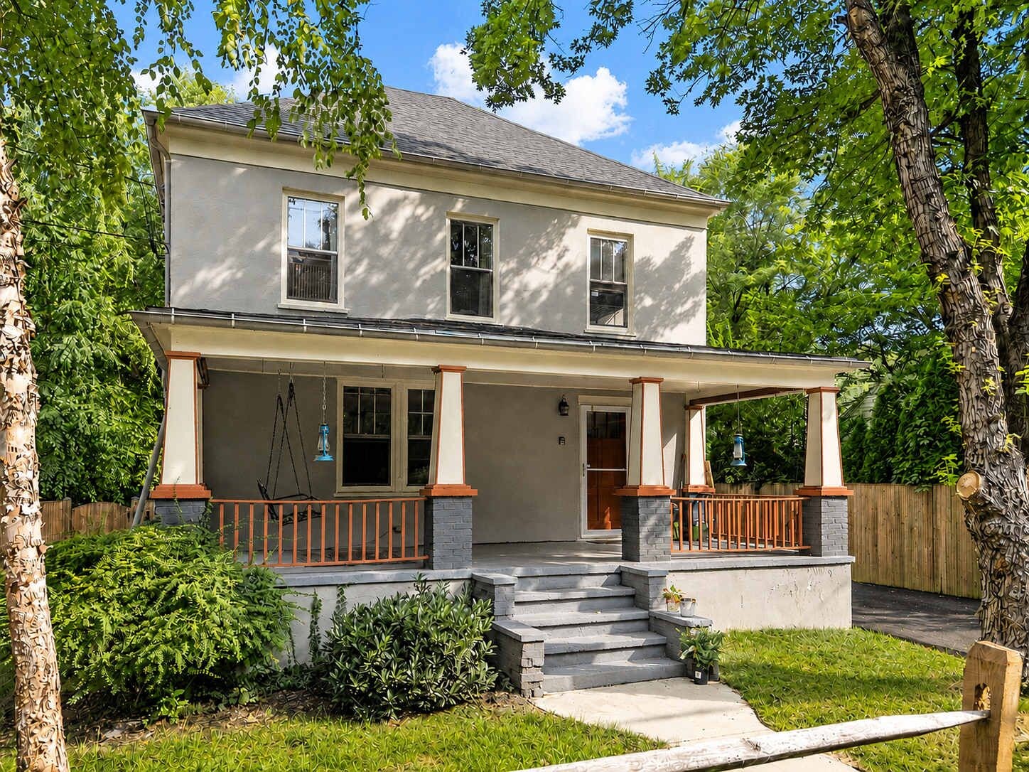 A two-story house with a porch, steps leading to the entrance, and a small garden area.