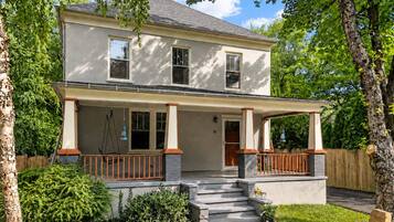 A two-story house with a porch, steps leading to the entrance, and a small garden area.