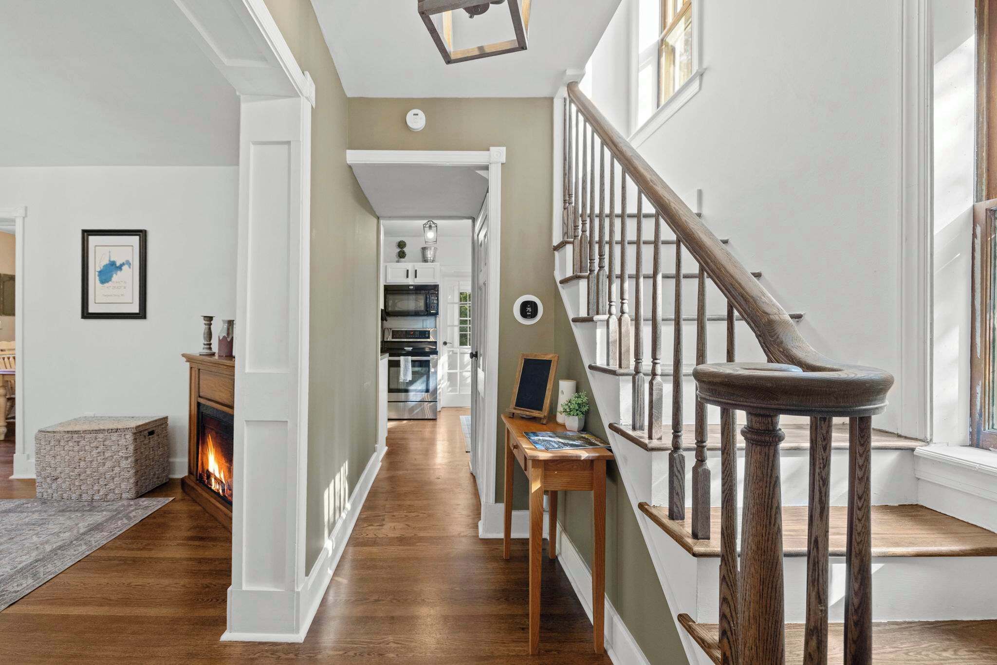 A hallway with a staircase, a fireplace, and a kitchen area in the background.