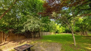 A backyard with a stone patio, a grill, and a wooden fence.