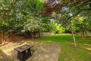 A backyard with a stone patio, a grill, and a wooden fence.