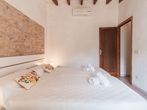 A bedroom with a stone wall, a wooden door, and a bed with white bedding and floral pillows. - Can Tianet by Interhome (Randa)