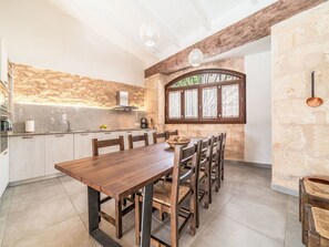 A modern kitchen with a wooden dining table, stone backsplash, and a large window with decorative iron bars. - Can Tianet by Interhome (Randa)