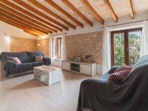 A living room with a stone wall, wooden beams, a sofa, a coffee table, and a TV stand. - Can Tianet by Interhome (Randa)