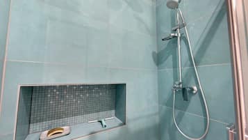 A bathroom with a shower, a tiled wall, and a shelf with a pair of slippers.