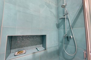 A bathroom with a shower, a tiled wall, and a shelf with a pair of slippers. - Apartment 'Le Bédat' with Mountain View, Balcony and Wi-Fi (Bagnères-de-Bigorre)