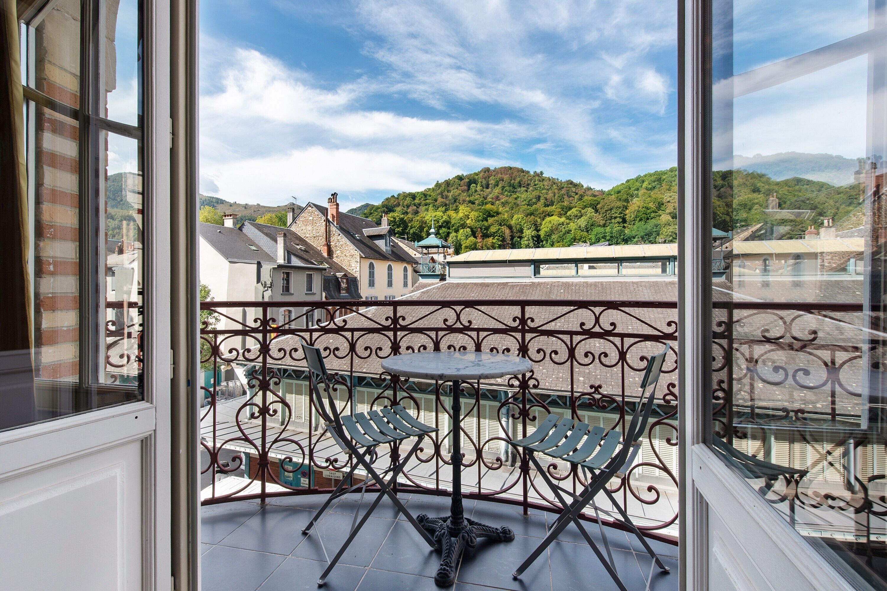 Ein Balkon mit Tisch und Stühlen, der auf eine Stadt mit Gebäuden und einem Hügel blickt.