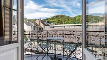Ein Balkon mit Tisch und Stühlen, der auf eine Stadt mit Gebäuden und einem Hügel blickt.