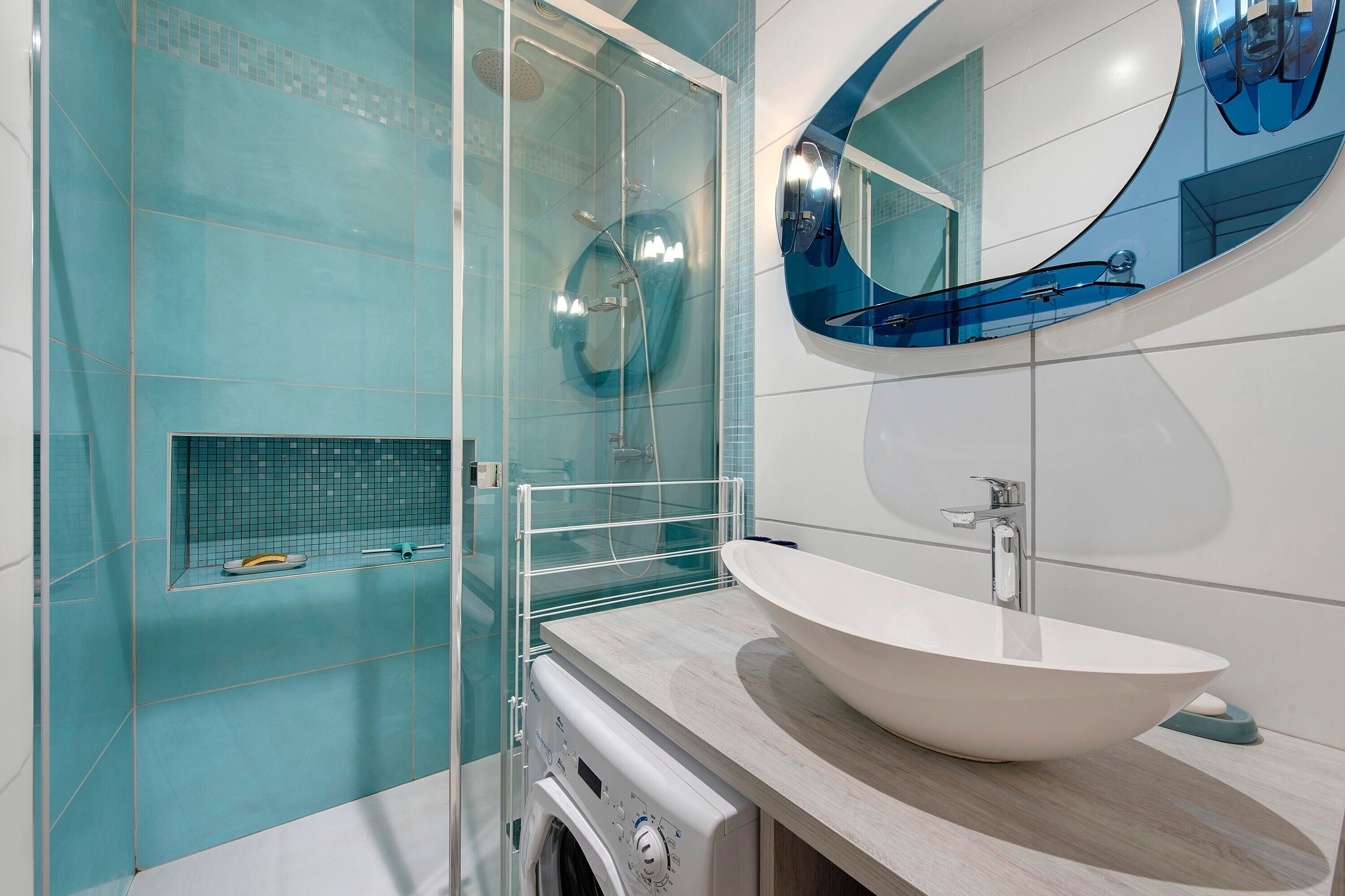 Une salle de bain moderne avec un grand lavabo ovale, une cabine de douche en verre et un lave-linge encastré.