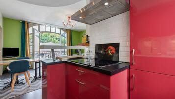 A modern kitchen with red cabinets, a black countertop, and a stainless steel range hood.