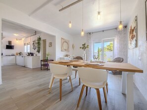 A modern kitchen with white cabinets, a dining area with a wooden table and white chairs, and a large window providing natural light. - Villa Pipa by Interhome (Deltebre)