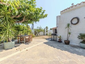 An outdoor patio with a table and chairs, surrounded by potted plants and a white wall with a wreath. - Villa Pipa by Interhome (Deltebre)