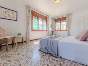 Quarto com cama, uma mesa pequena, uma cadeira e espelho fixado na parede.