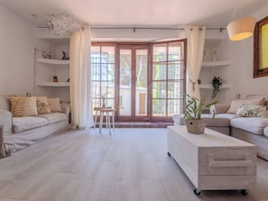Uma sala de estar espaçosa com uma grande janela, um conjunto de sofás, uma mesa de centro e uma planta decorativa.