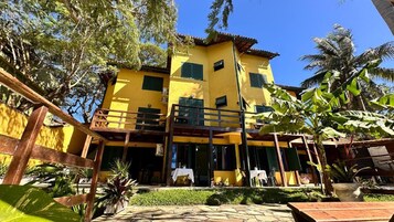 Un edificio amarillo de dos pisos con un balcón, rodeado de vegetación tropical.