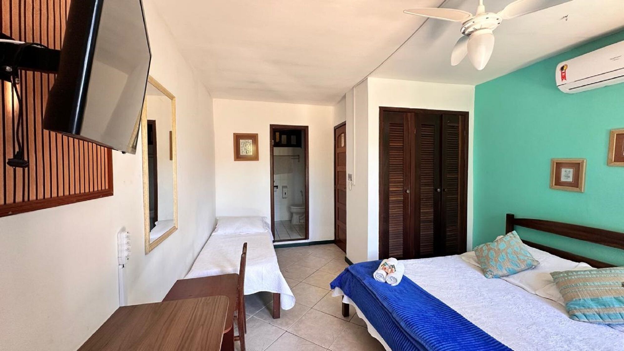 A hotel room with two beds, a TV mounted on the wall, a ceiling fan, and a bathroom visible through an open door.