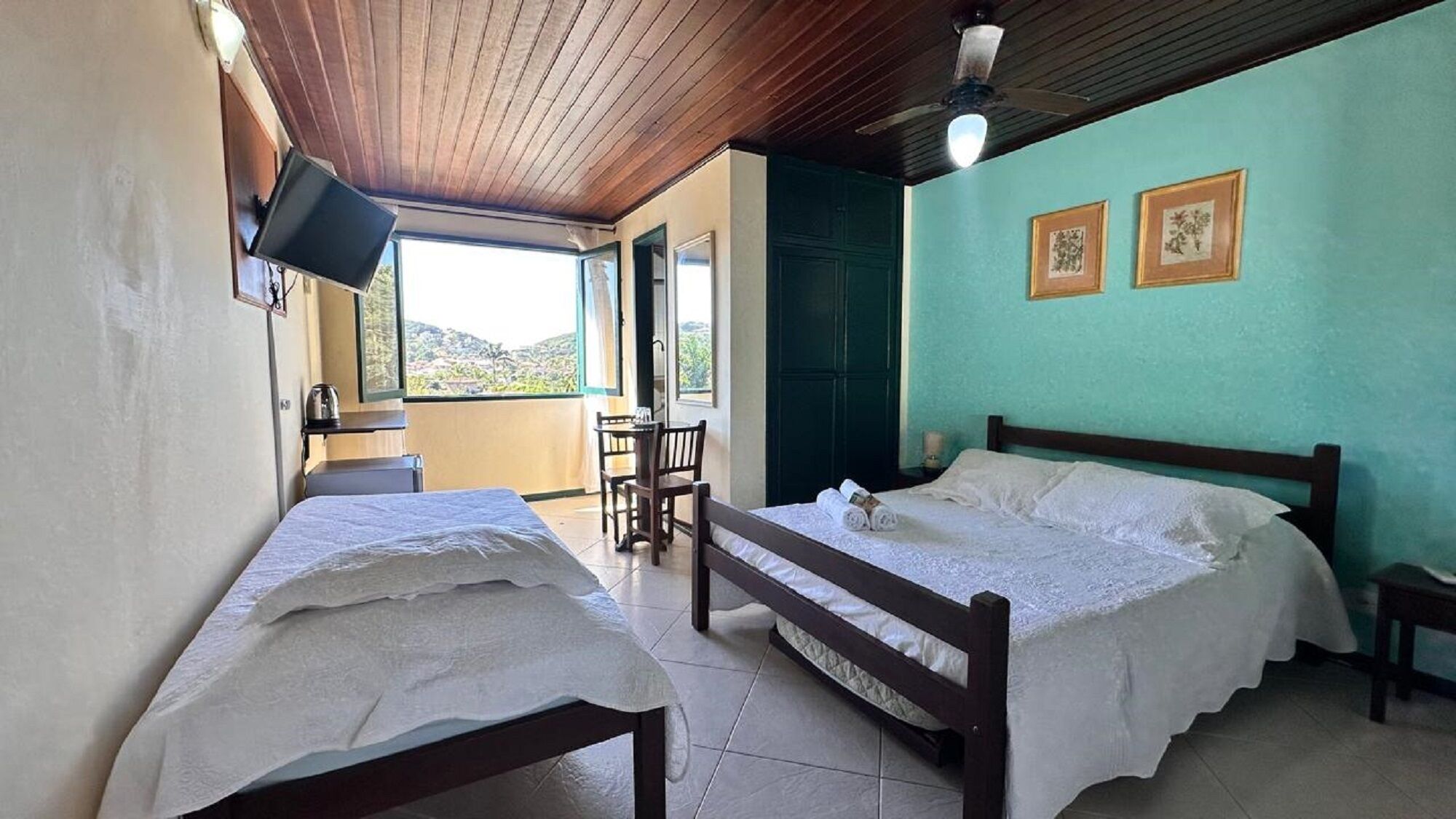Ein Zimmer mit zwei Betten, einem an der Wand befestigten Fernseher und Blick ins Freie.