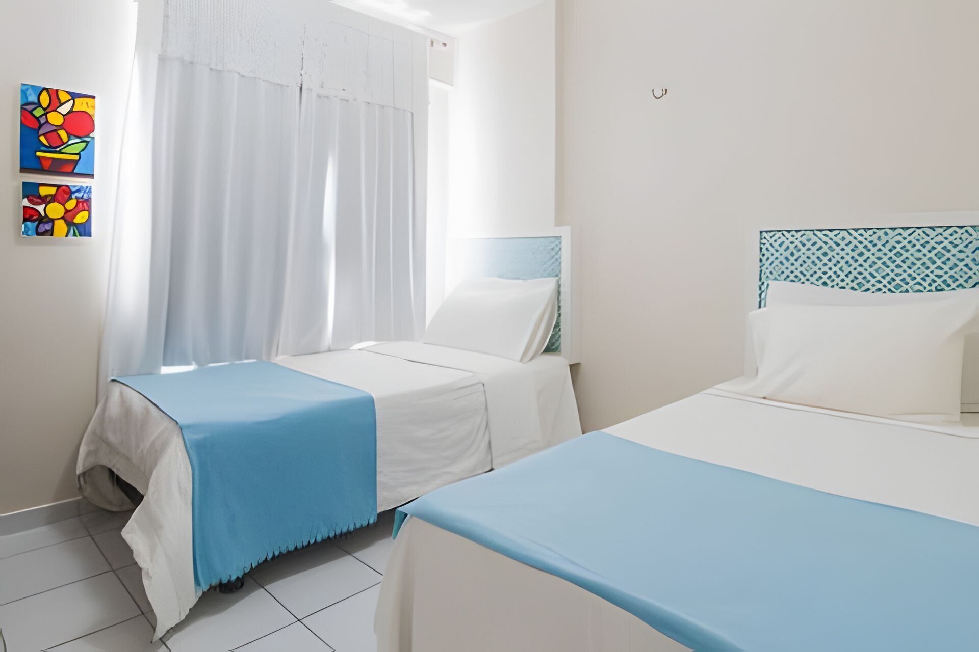 Habitación de hotel con dos camas, una ventana con cortinas y una pared con obras de arte coloridas.